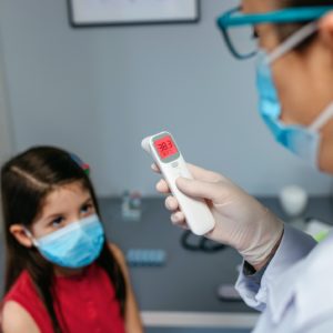 Female pediatrician looking at infrared thermometer after taking temperature to a girl